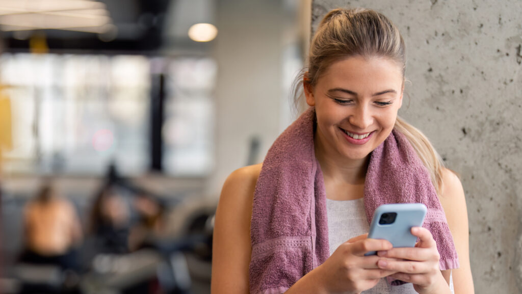 Woman at a health club checking her phone looking happy and healthy