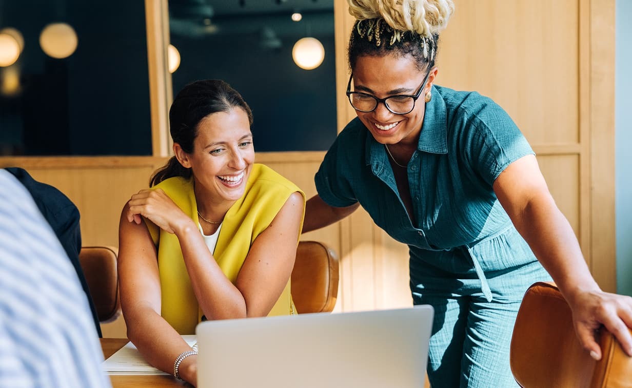 two women smiling and looking at a laptop screen