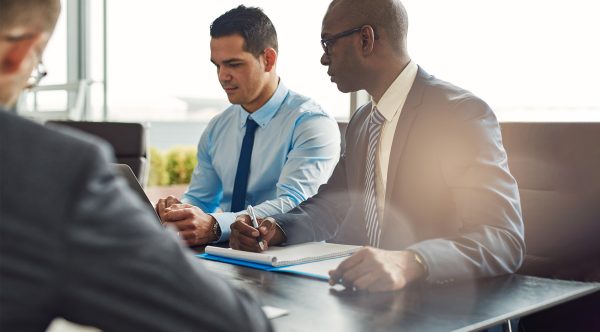 Business executives in a management meeting seated at a table with paperwork and a laptop with focus to a Hispanic and African American man