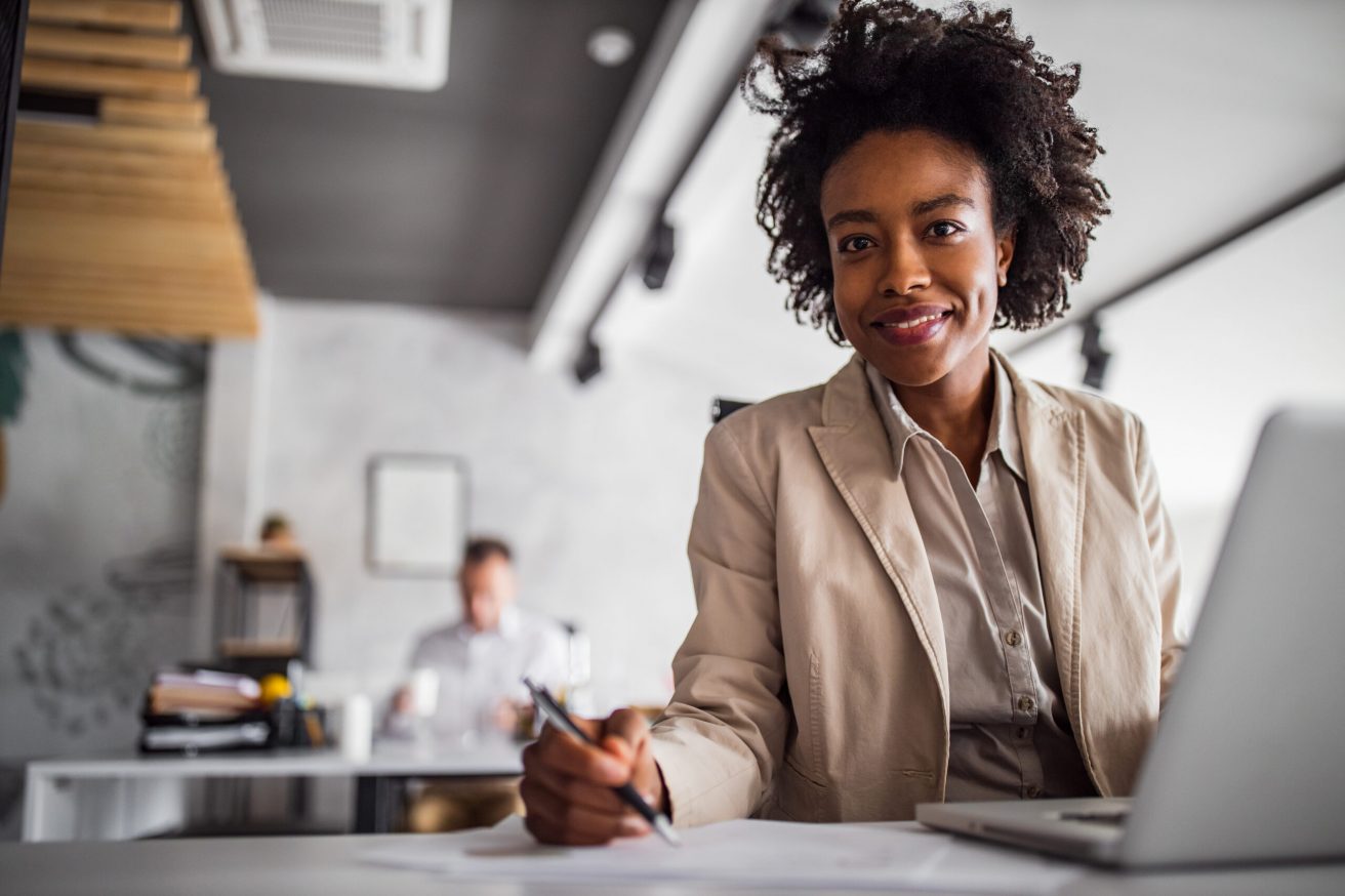 Business woman looking and posing for camera, while writing notes in her notebook.