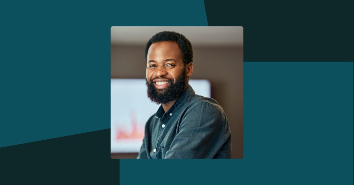 Man in teal shirt smiling at camera in an office