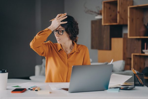 Frustrated Italian female employee stressed about mistake or problem with computer, got bad news from office. Tired nervous spanish woman working remotely online from home. Pressure at work concept