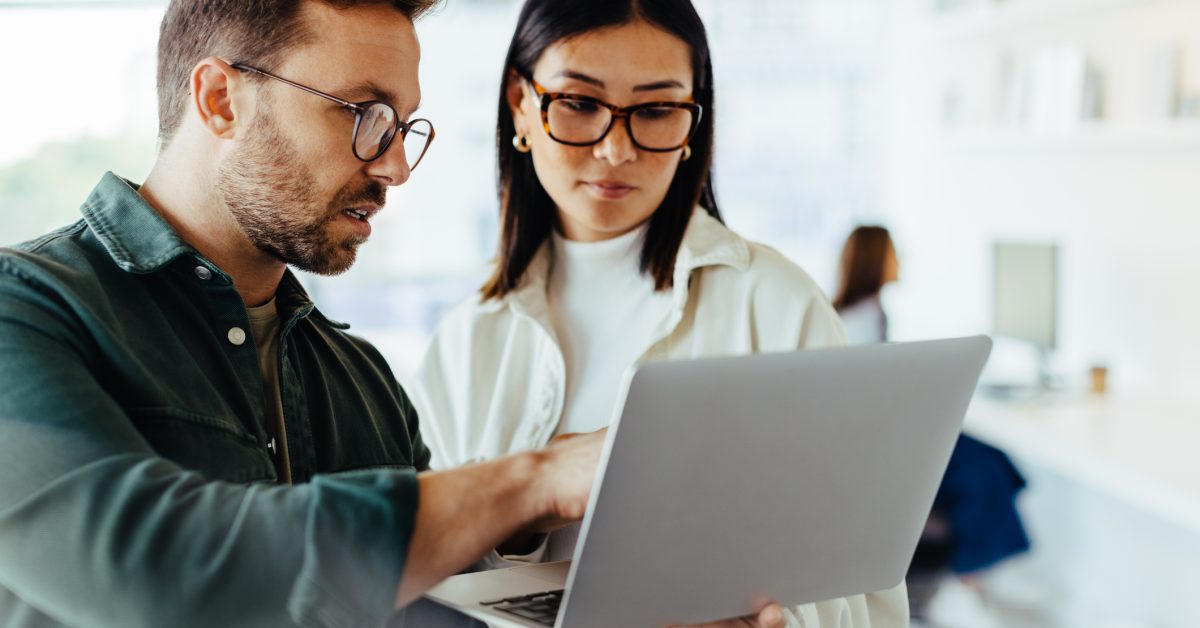 Two people comparing notes while looking at a laptop computer.