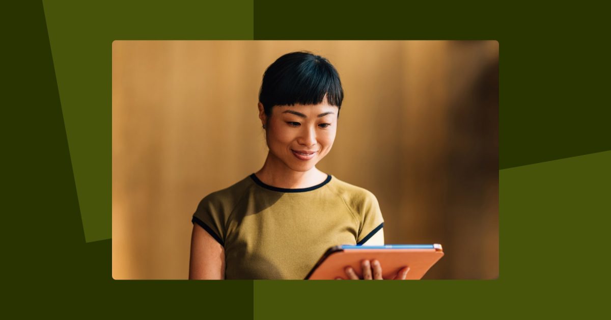Photo of woman smiling and standing looking down at orange tablet she is holding in her hands